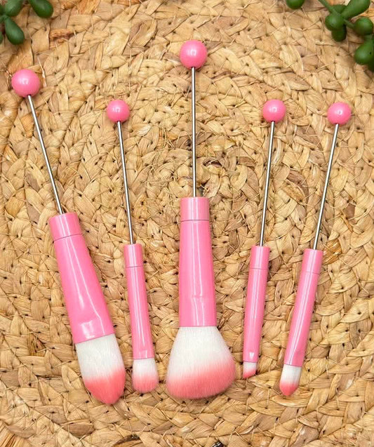 Five pink-handled makeup brushes with long metal stems and pink pom-pom tops, 