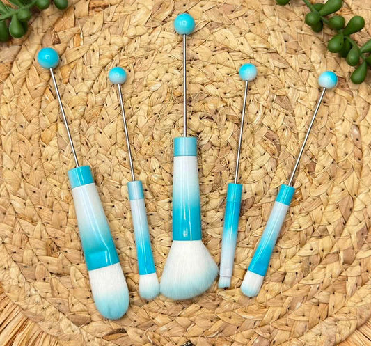 Five makeup brushes with blue and white gradient handles and silver metal stems, 